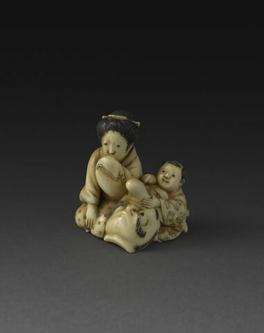 Netsuke : femme et enfant entourant un masque grotesque.