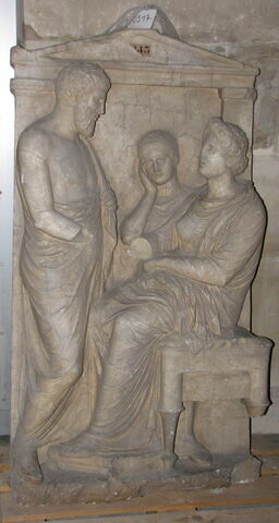 Tirage d’une stèle funéraire attique
Le haut-relief représente un homme (Thraséos du dème de Perithoidai), debout de trois-quarts et vêtu d'un himation, serrant la main (dexiosis) d'une femme (Evandréia), assise sur un tabouret, vêtue d'un chiton et d'un himation. Entre eux, à l'arrière-plan apparaît une petite fille (servante) la tête appuyée sur la main droite en signe d'affliction. Une inscription en grec, gravée sur l'architrave, indique les noms des personnages.
Le moulage ne présente ni les mains droites de la femme et de l'homme debout, ni le pied arrière du siège.