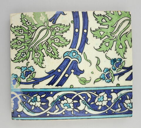 Carreau à décor de tiges ondulantes porteuses de palmettes feuillues, fleuries et à coeur de tulipe. Bordure à rinceau fleuri et de fleurons bifides sur fond bleu