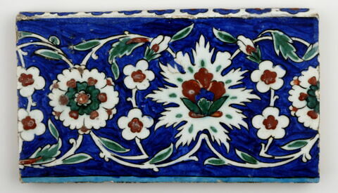 Carreau de bordure aux lotus alternant avec des fleurettes et des rosettes sur fond bleu