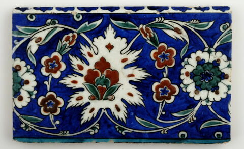 Carreau de bordure aux lotus alternant avec des fleurettes et des rosettes sur fond bleu